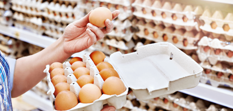 A woman feels eggs from a shelf, presumably to assess their freshness.